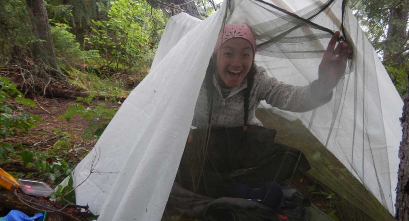 a person smiles from under a tarp shelter amongst trees on an outward bound course